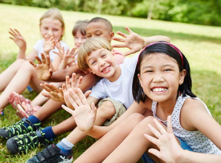 there is a group of children in a park smiling and waving at the camera.