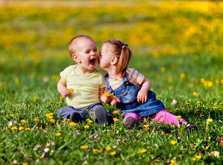 Two kids sitting in a field.